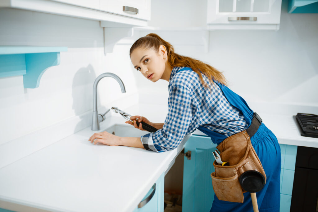 Cute female plumber in uniform fixing faucet